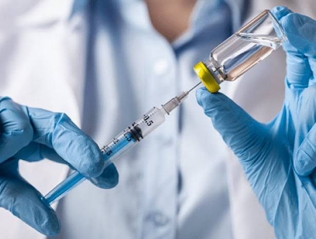 Profissional de luvas preparando uma seringa a partir de um frasco de medicação